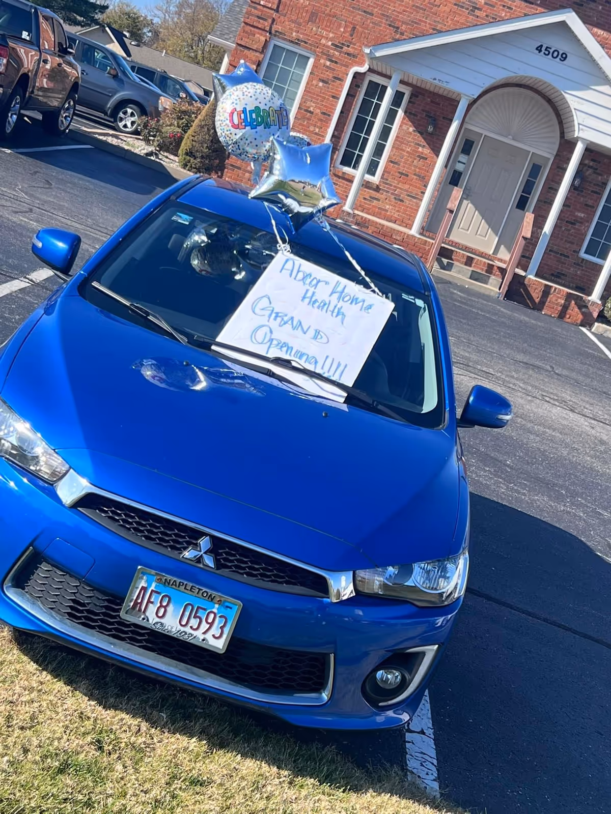 Blue car parked in front of a brick building with Abcor Home Health signage and balloons.