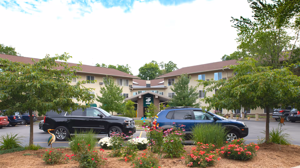 Exterior front of a senior living building with cars parked in front and flowering landscaping in the foreground.