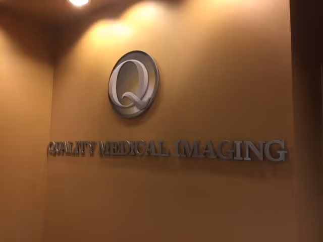 Indoor wall features a metallic Quality Medical Imaging sign with circular logo.