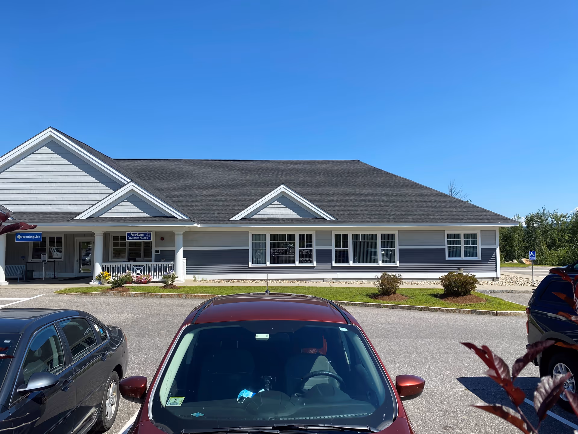 Single-story blue-gray building with white trim, entrance, and parked cars in front.