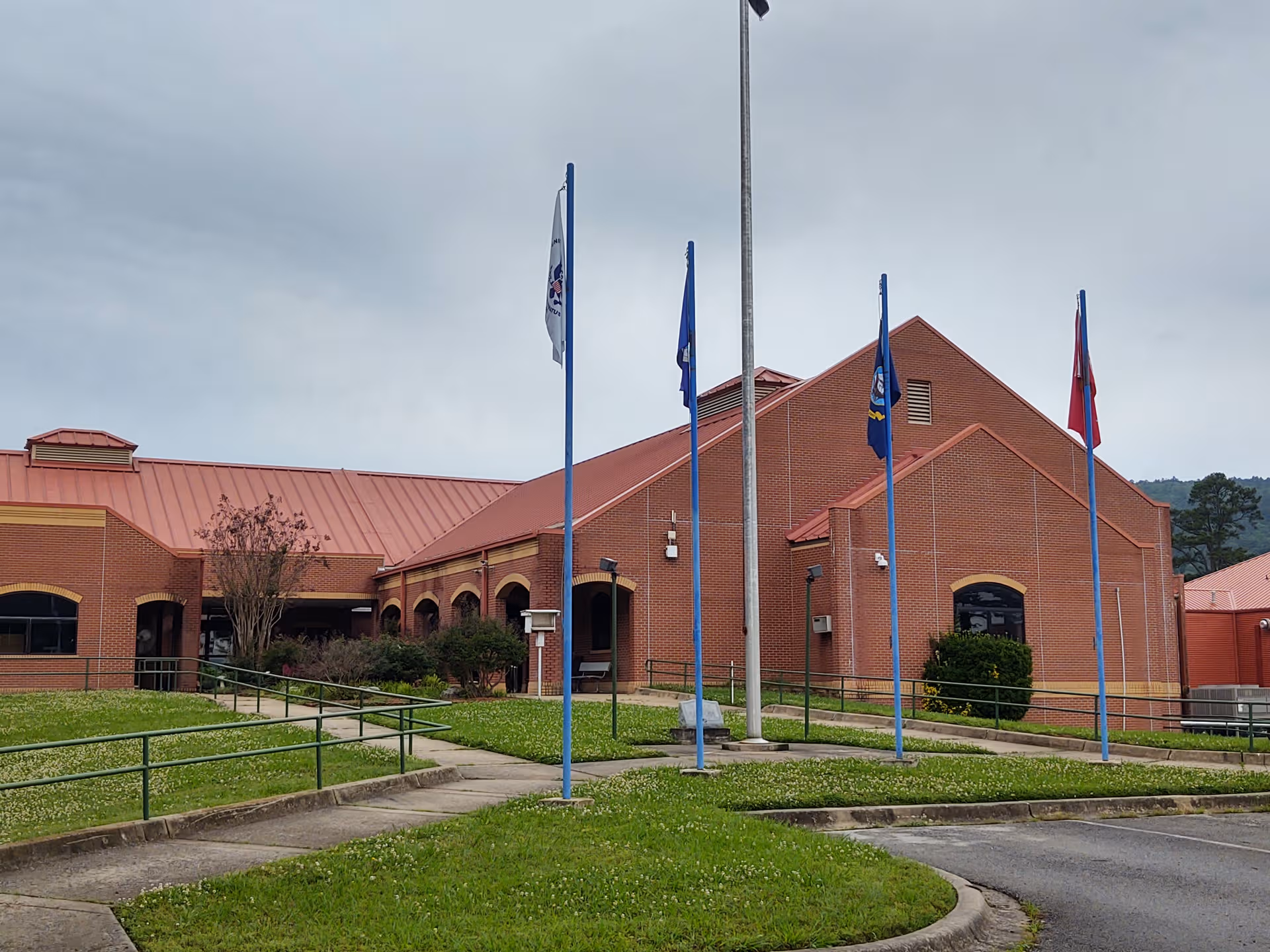 Brick Oklahoma Veterans Center building with red roof, flags, and curved walkway entry.