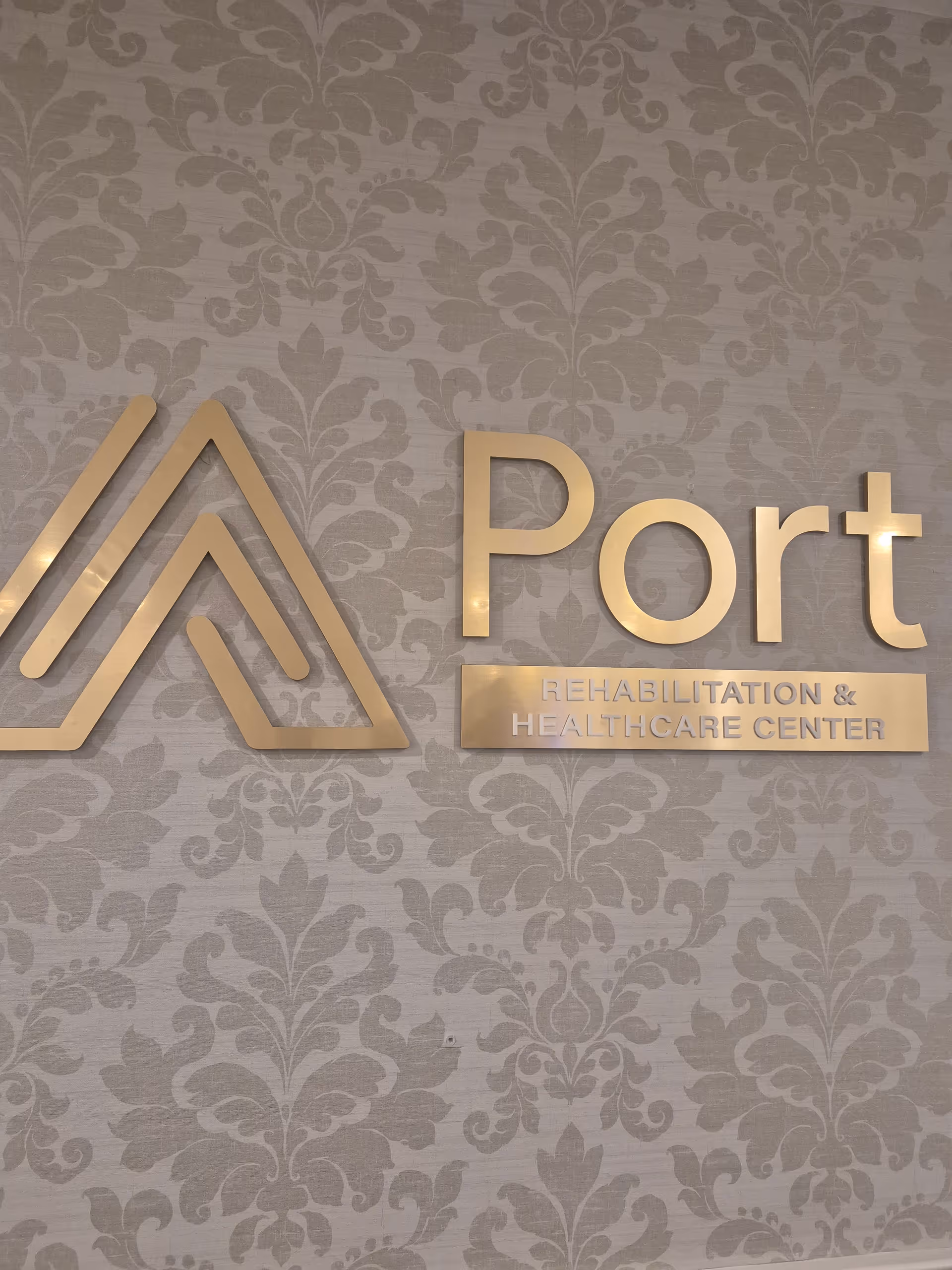 Interior wall with Port Rehabilitation & Healthcare Center logo on ornate patterned wallpaper.