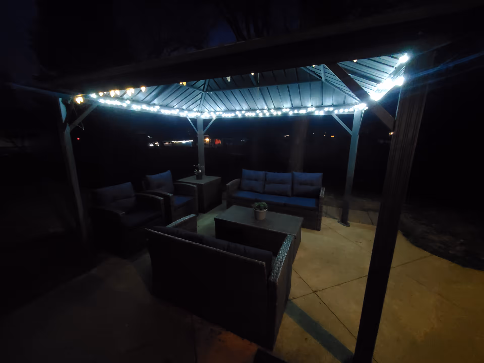 Outdoor seating under a gazebo at night with string lights and cushioned furniture.