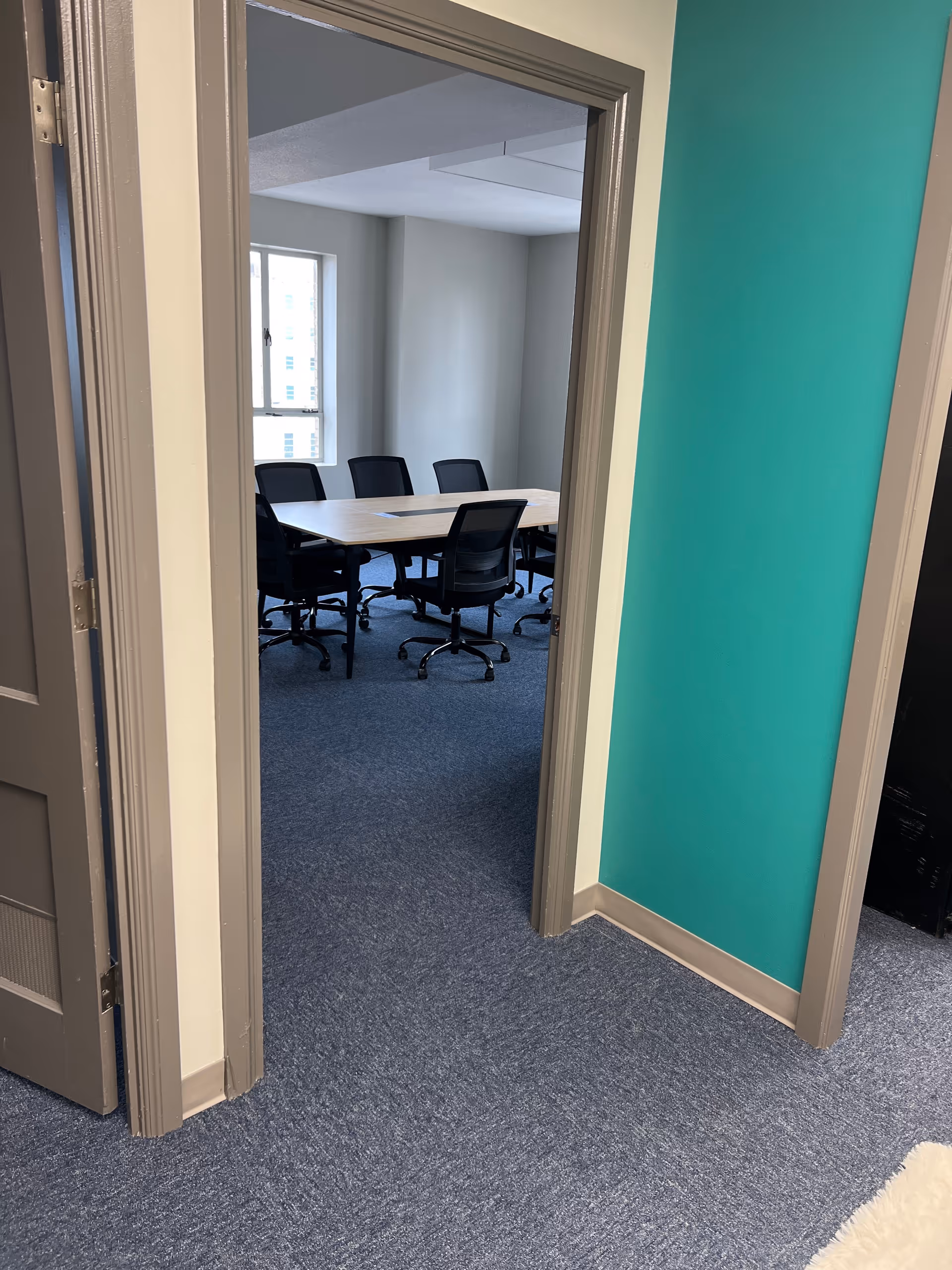 Doorway opens to a conference room with a long table and black office chairs.