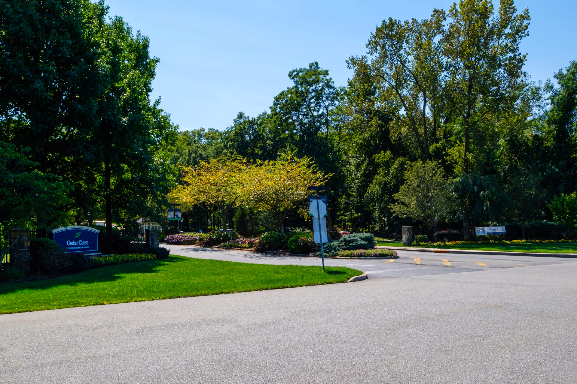 Entrance to Cedar Crest facility with a paved road, green lawns, trees, and landscaped bushes under a clear blue sky.