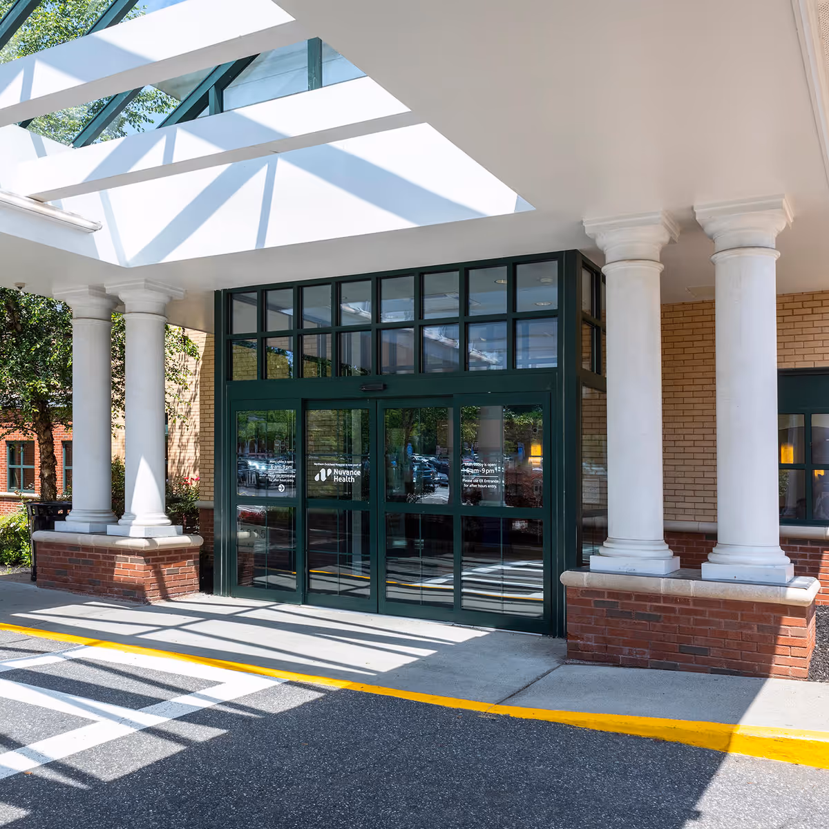 Entrance to a medical facility with green-framed glass doors, white columns, and brick exterior.