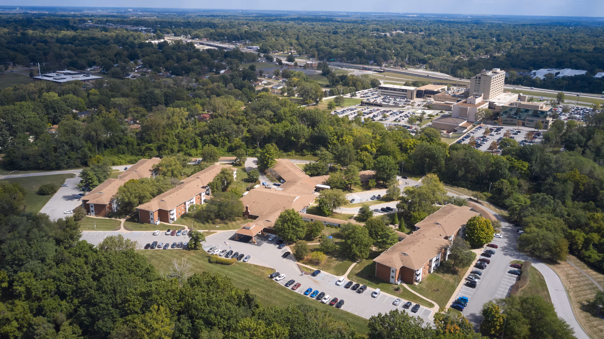 Aerial view of Village North Retirement Community campus with brick buildings, parking lots, and trees.