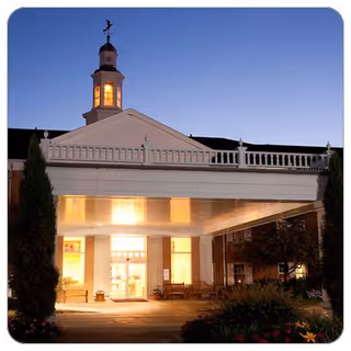 Exterior view of Copeland Oaks entrance with columns and a clock tower at dusk.