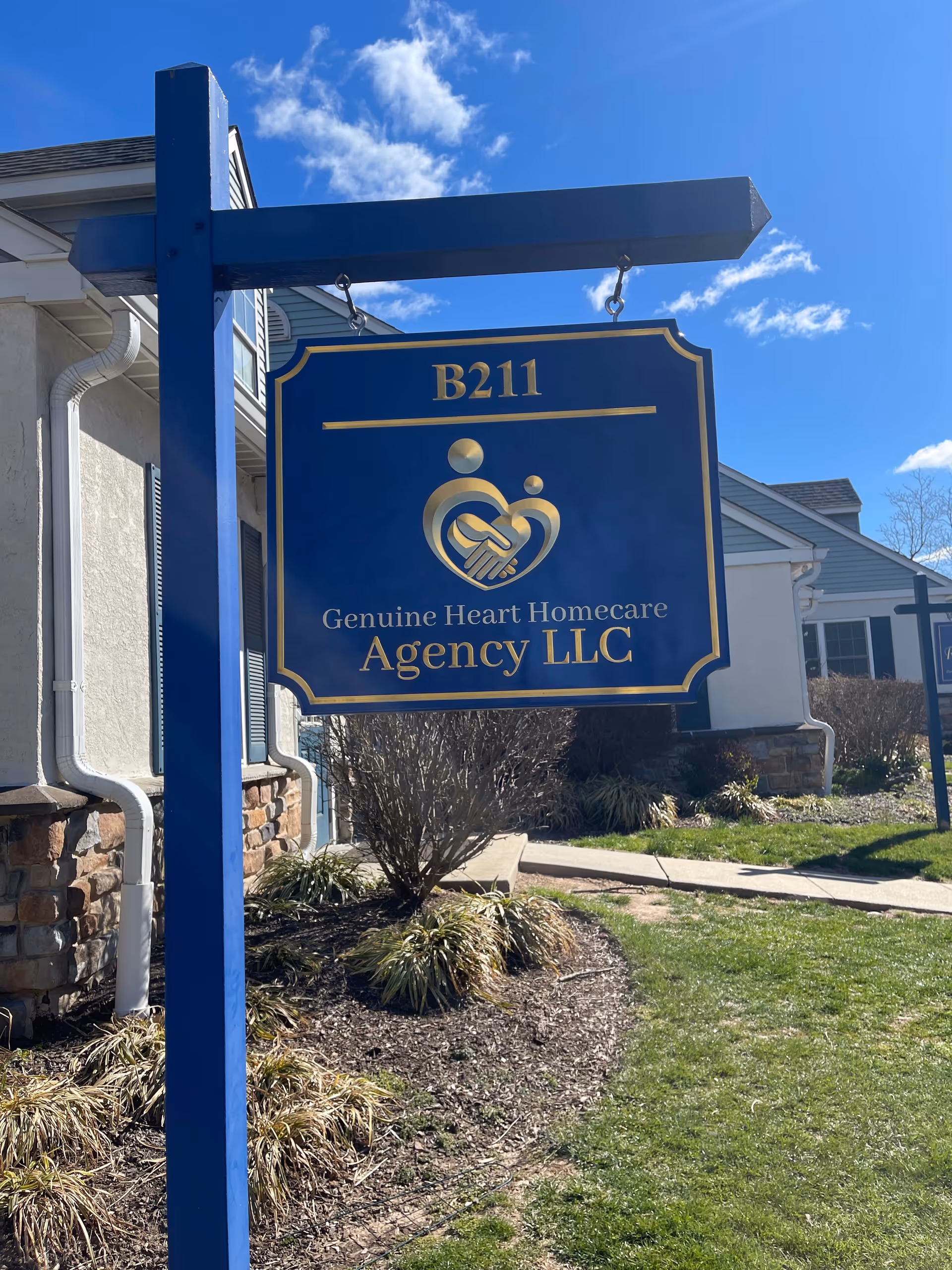 Blue sign for Genuine Heart Homecare Agency LLC outside a light-colored building.