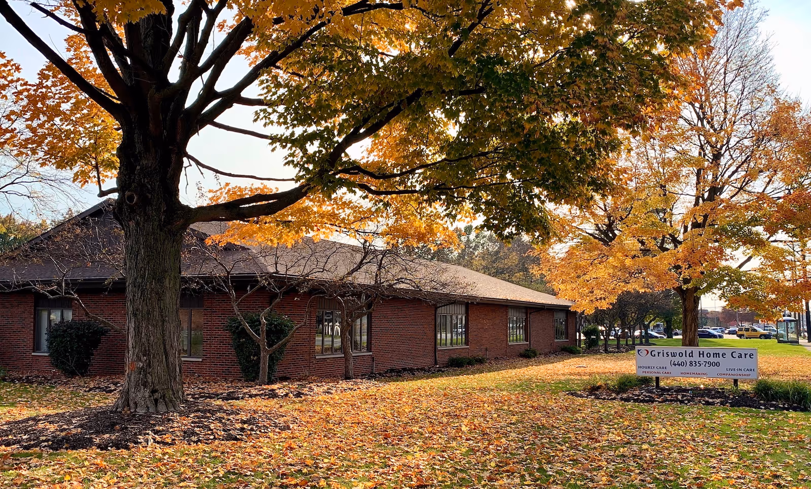 Brick senior care facility exterior with autumn trees and a Griswold Home Care sign.