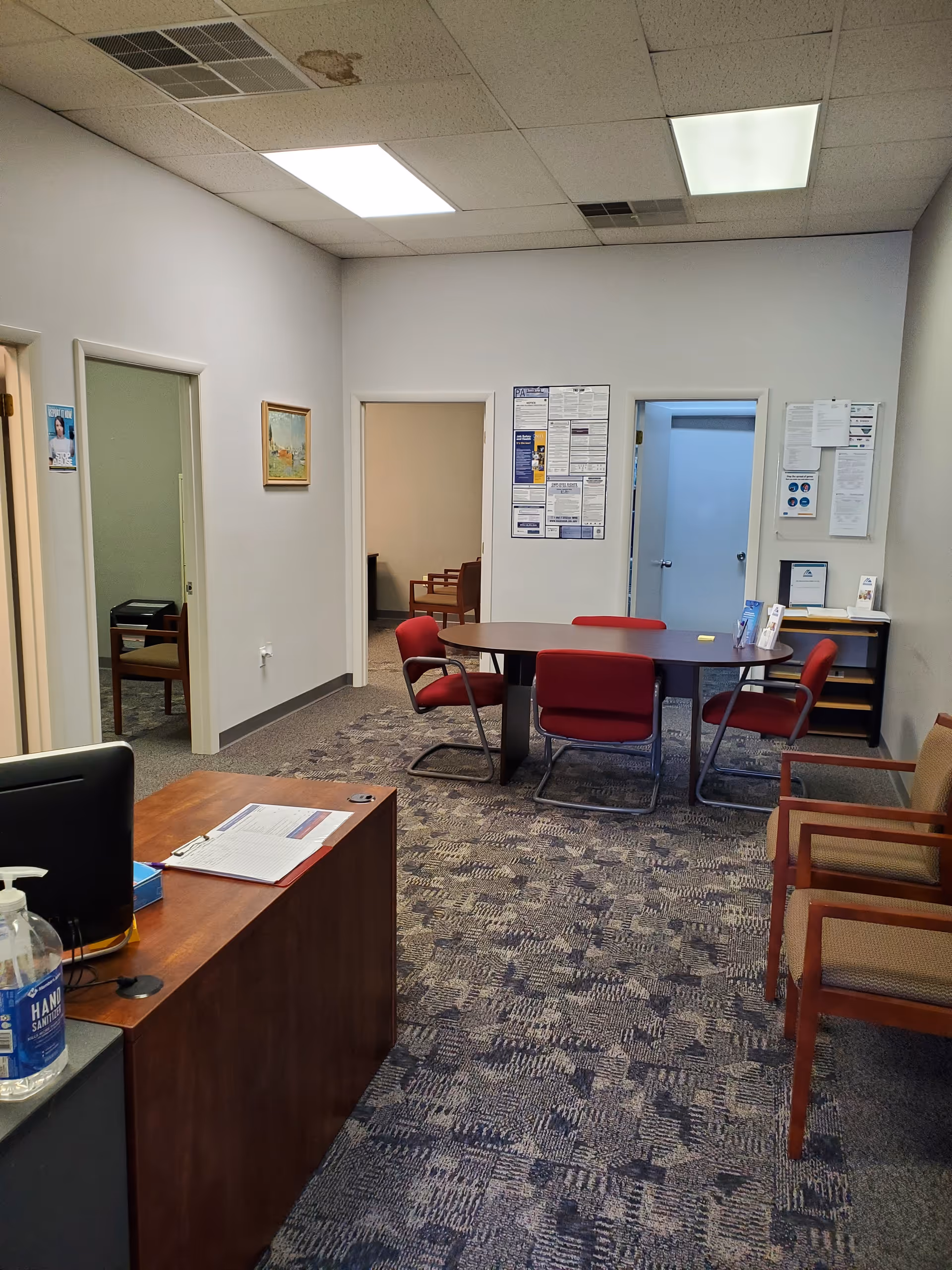 Office-like reception area with a desk, round table, red chairs, and bulletin boards.
