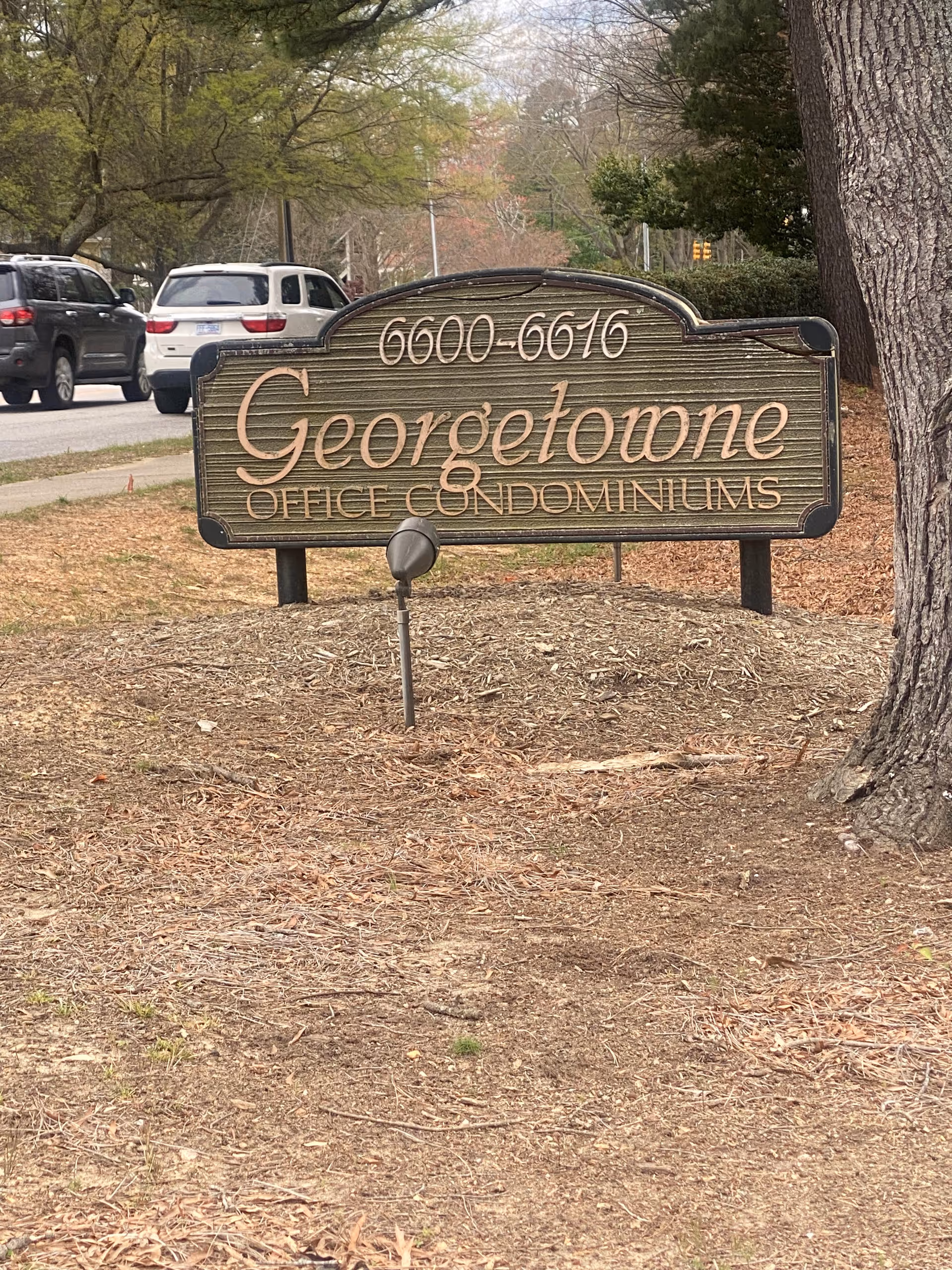 Outdoor sign reading Georgetown Office Condominiums, with mulch, trees, and parked cars nearby.