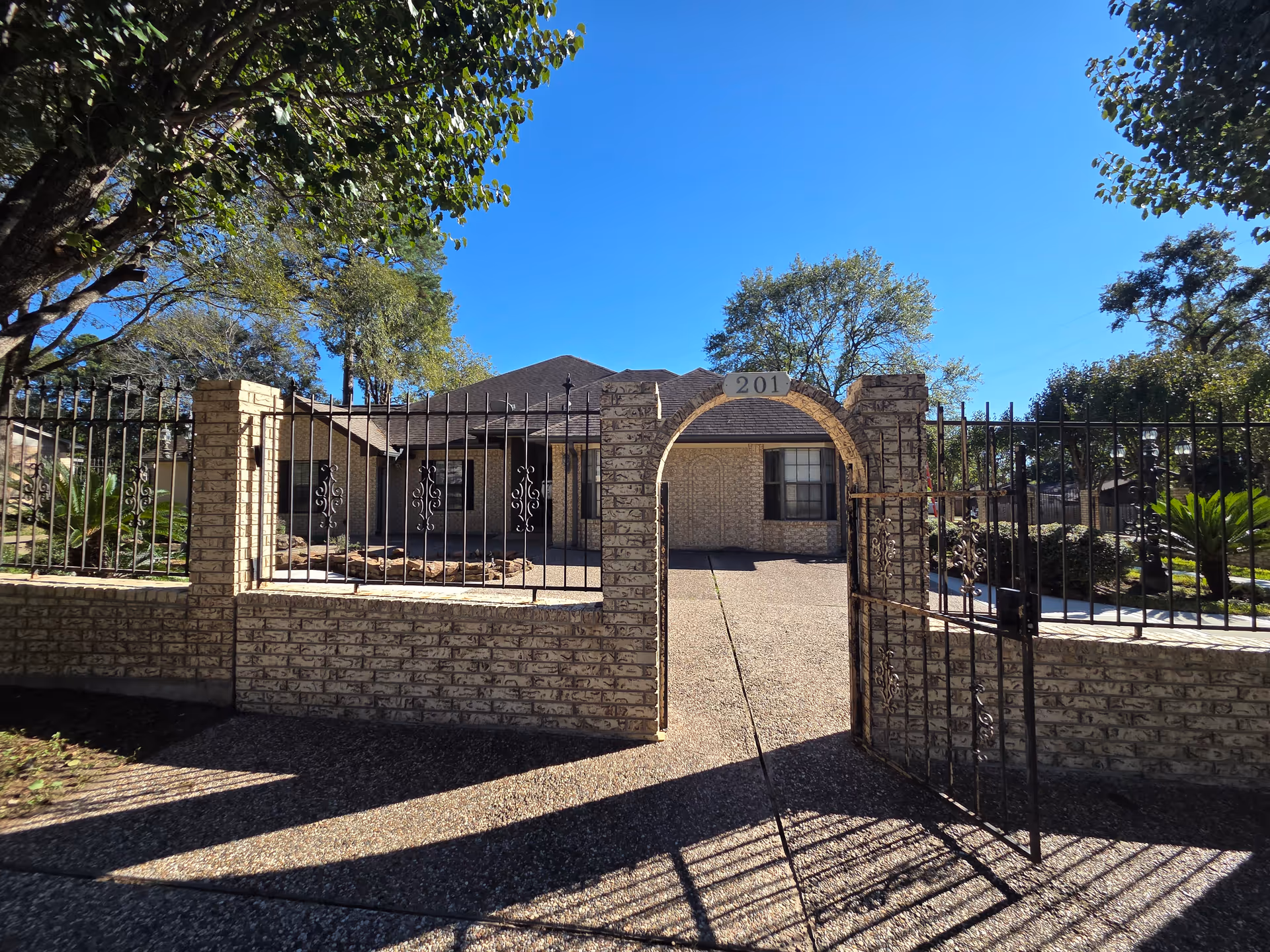 Stone gated entrance to Sunrise Senior Care Home with archway, driveway, and blue sky.