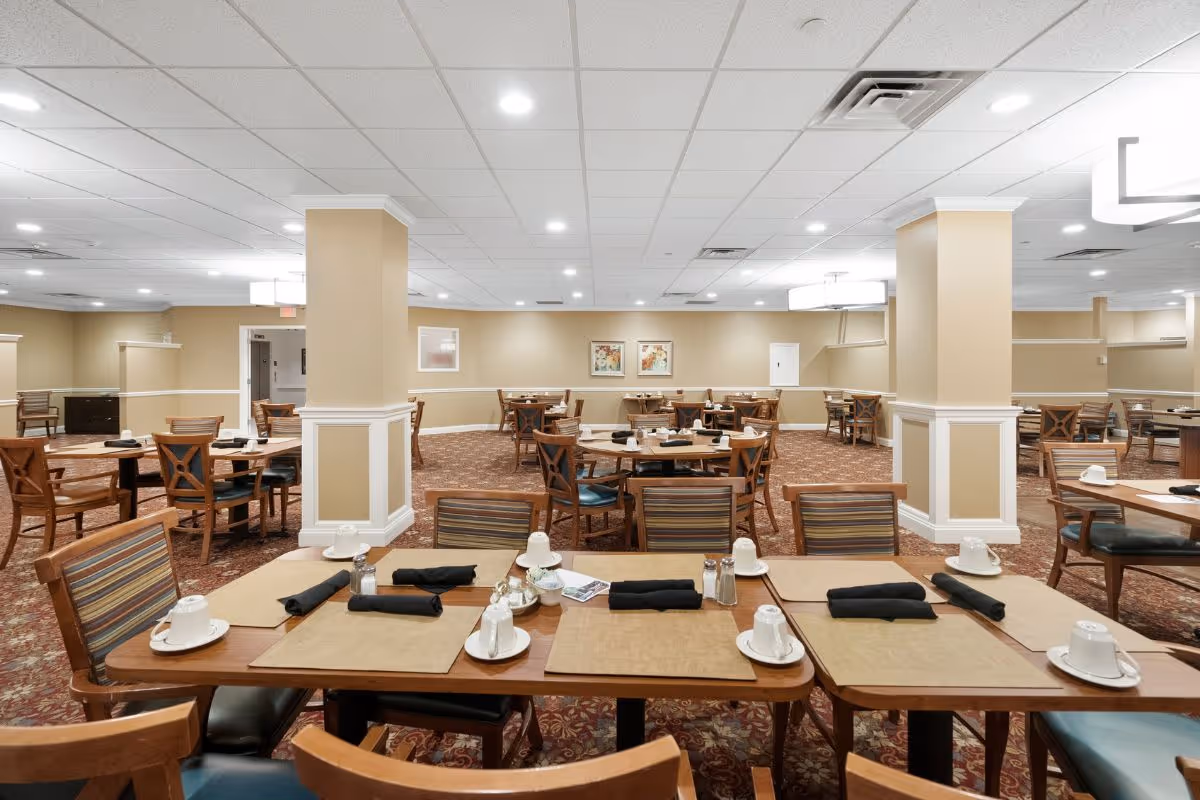 Spacious dining hall with many tables set for meals and beige-walled decor.