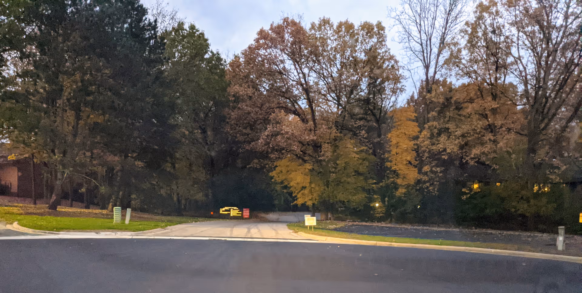 Front view of a road and autumn trees along a lawn near a care facility.