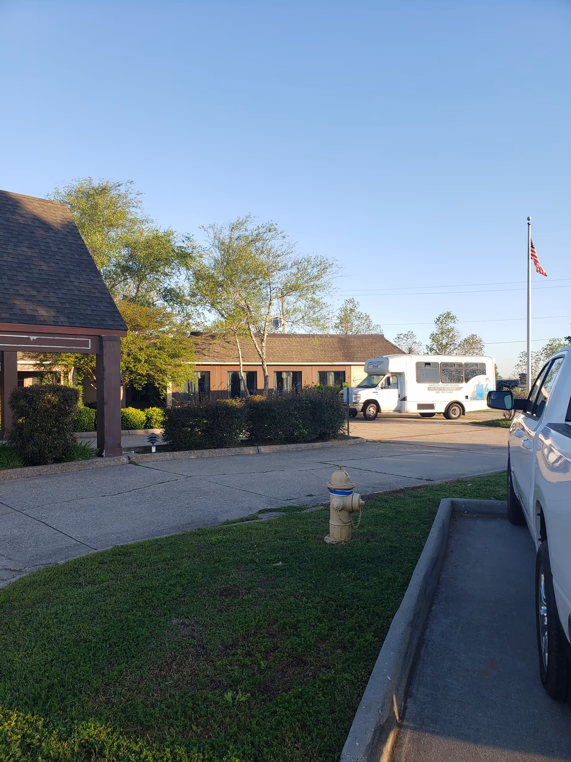 Exterior view of Garden Court Health and Rehabilitation Center with a bus, parking lot, and flag.