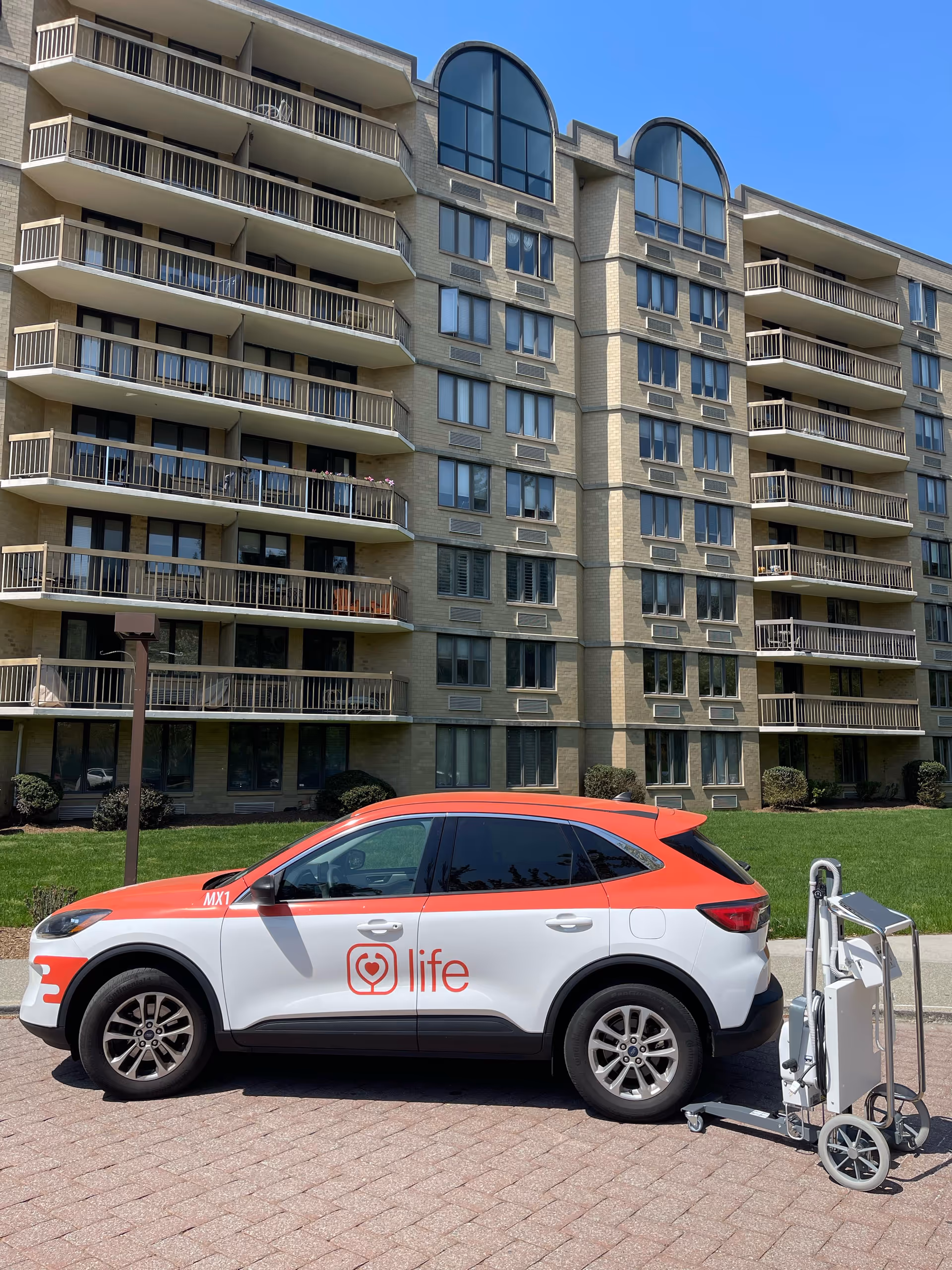 Multi-story residential building with balconies and a Life car parked outside.