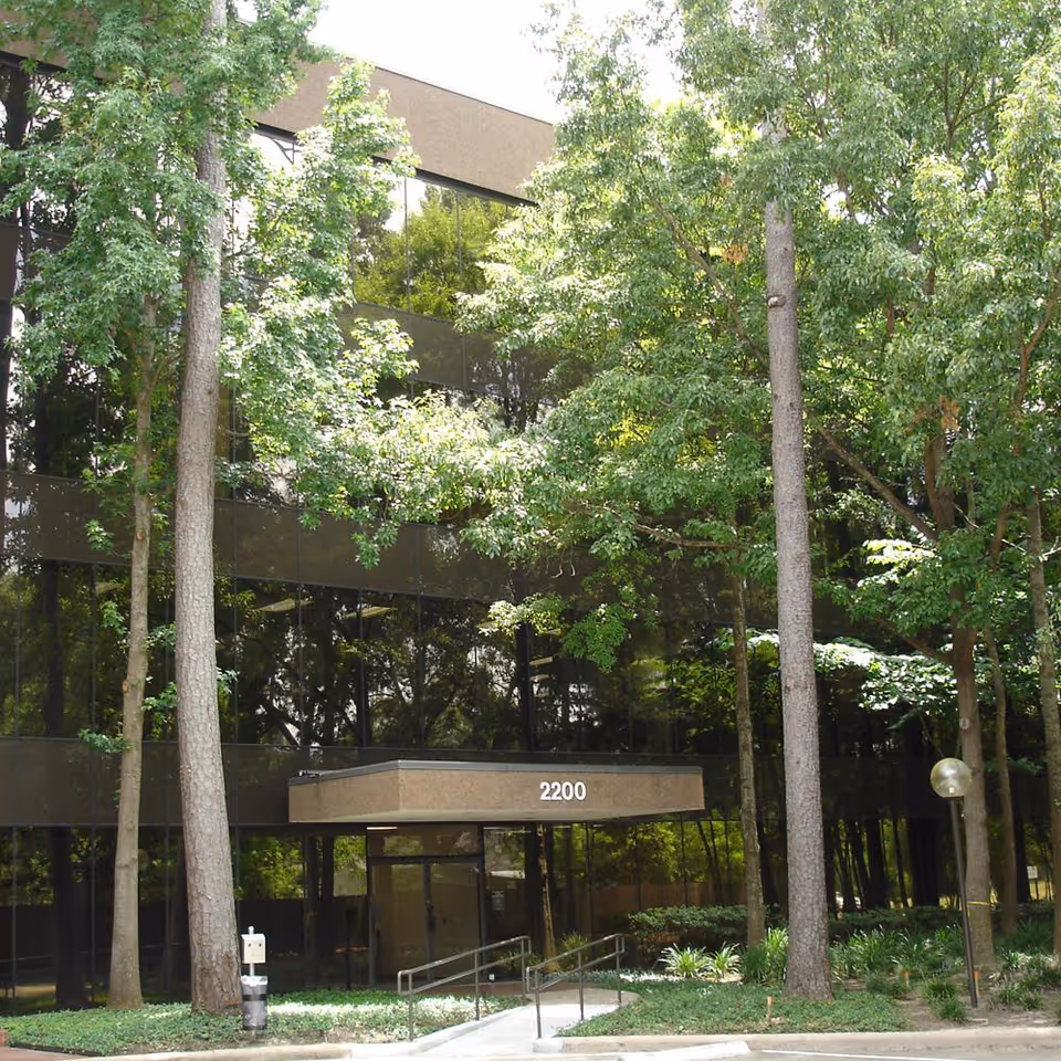 Exterior view of a glass-front building entrance surrounded by tall trees.