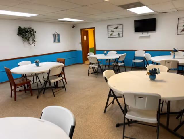 Bright dining room with round tables, white chairs, blue wainscoting, and ceiling lights.