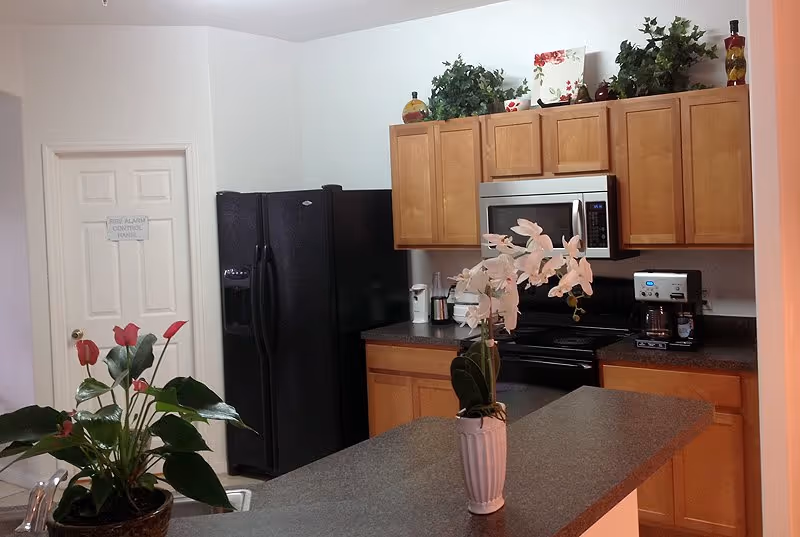 Kitchen area in a senior living facility with cabinets, appliances, and an orchid centerpiece.
