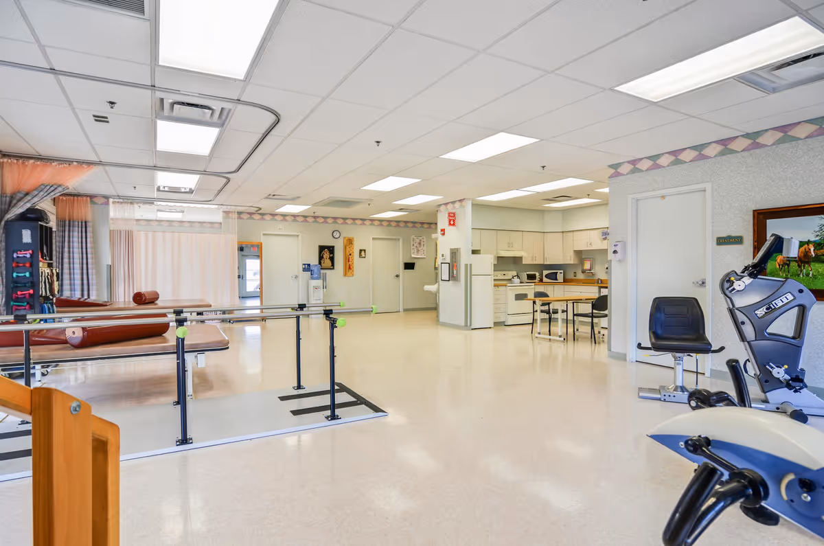 Bright rehabilitation gym in a senior living facility with exercise equipment and tables.