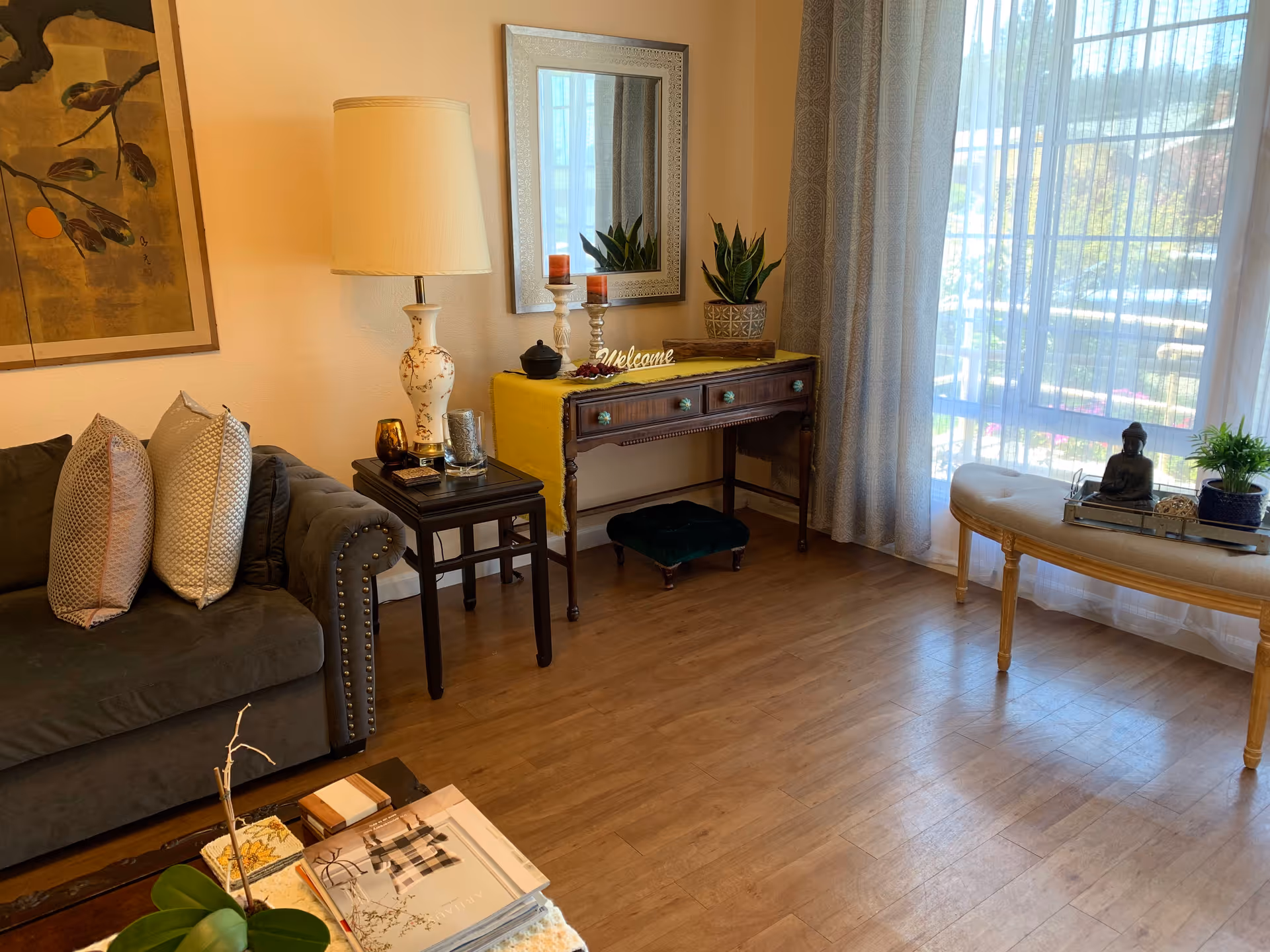 Living room in a senior facility with sofa, console table, lamp, and large window view.