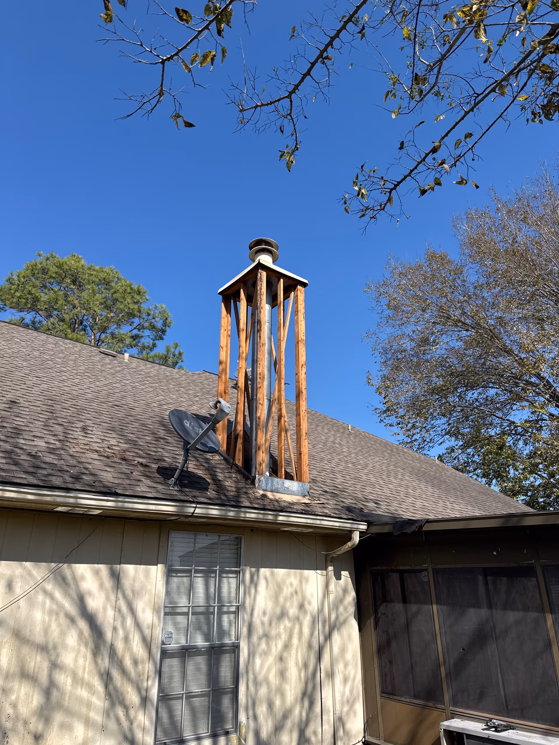 A brown shingle roof with a wooden chimney frame and satellite dish against a blue sky.