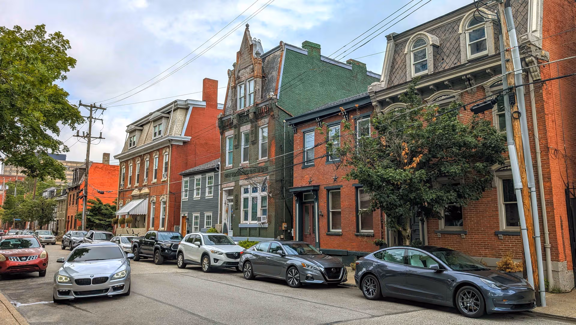 Row of brick townhouses along a tree-lined street with parked cars.