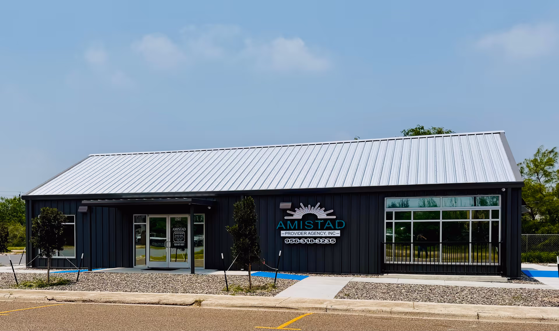 A dark modern building front housing Amistad Provider Agency, with metal roof and glass windows.