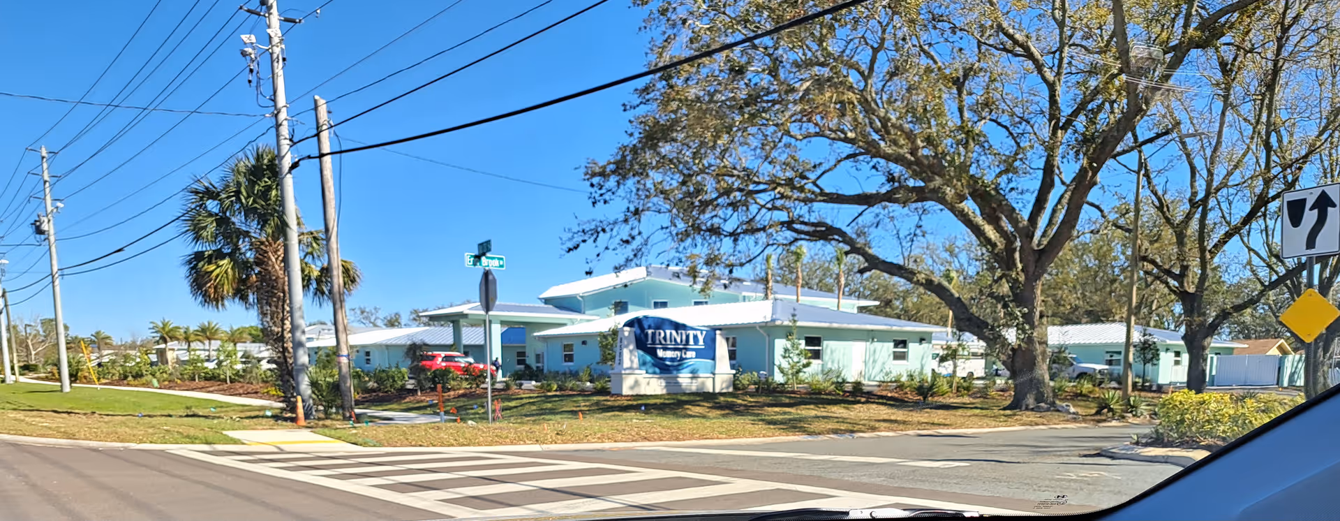 Exterior view of Trinity Memory Care building with a sign, trees, and a street intersection.