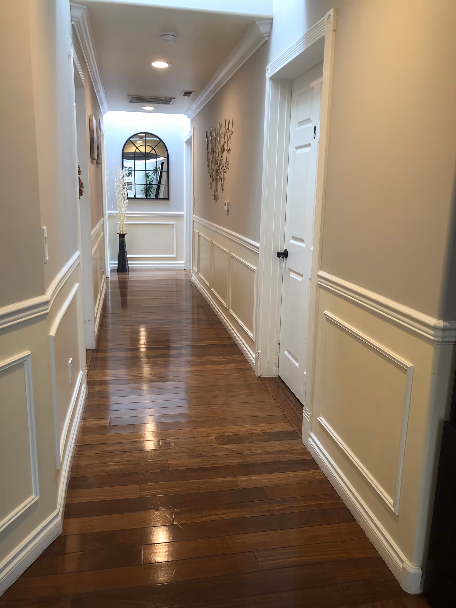 Long hallway in a senior living facility with wood floors, wainscoting, and decorative wall art.