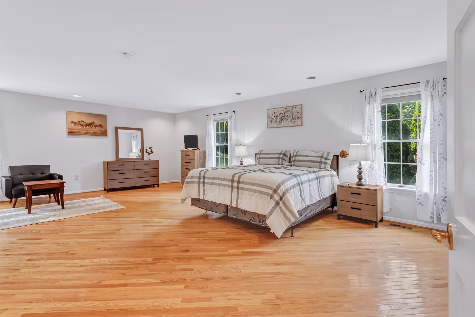 Spacious bedroom with a large bed, matching nightstands, dresser, and wooden floors.