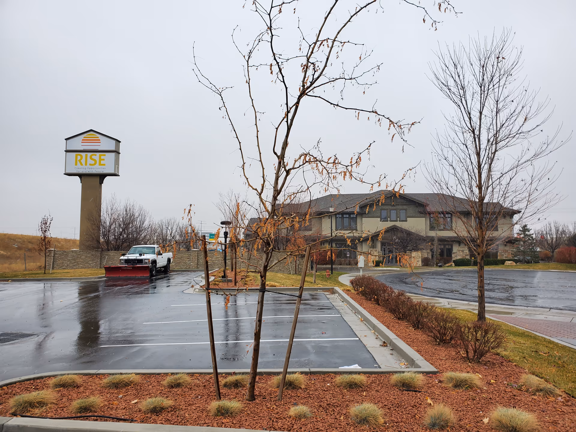 Wet parking lot in front of a Rise Services facility with a large sign.