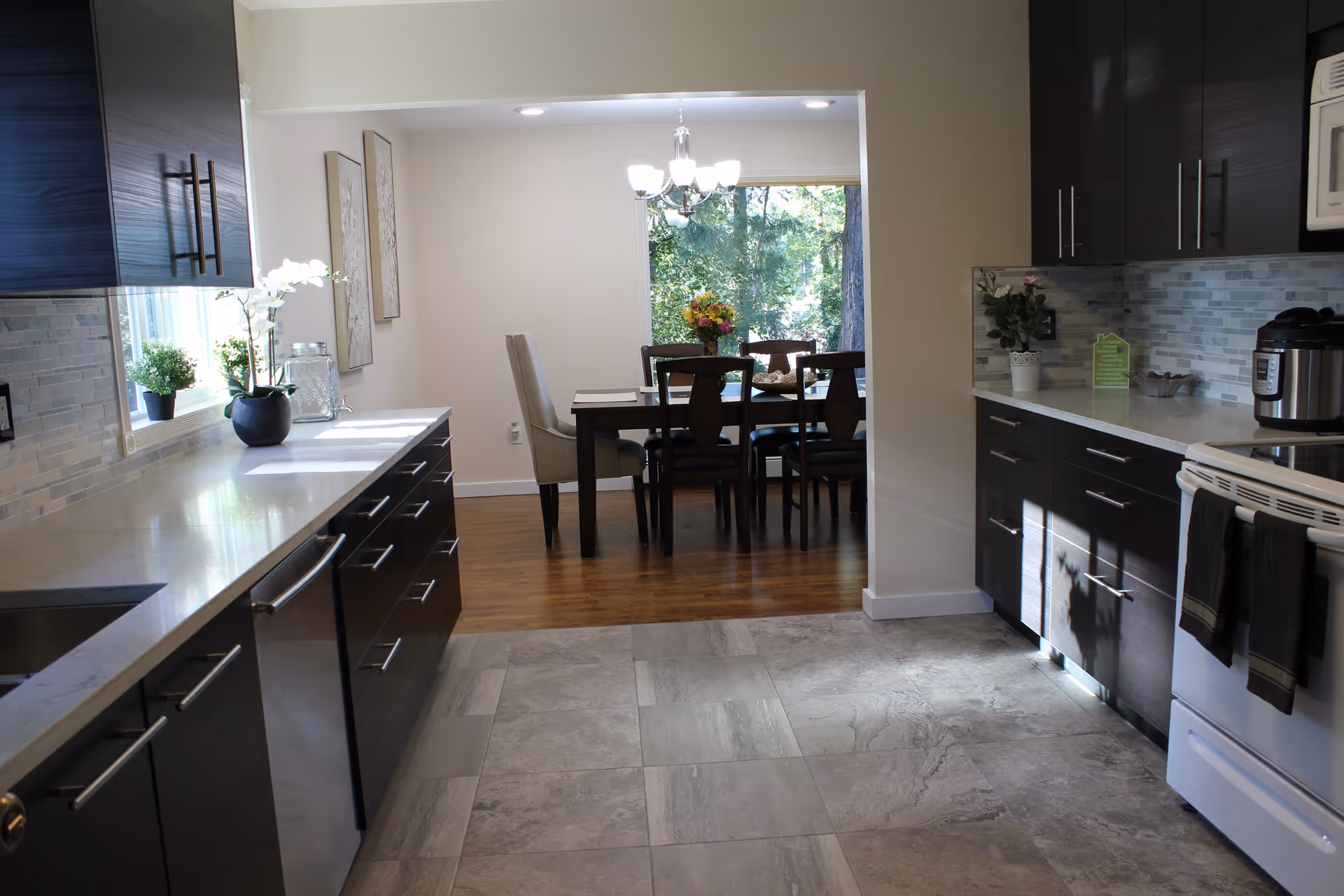 Modern kitchen leads into a dining room with a wooden table and chandelier.
