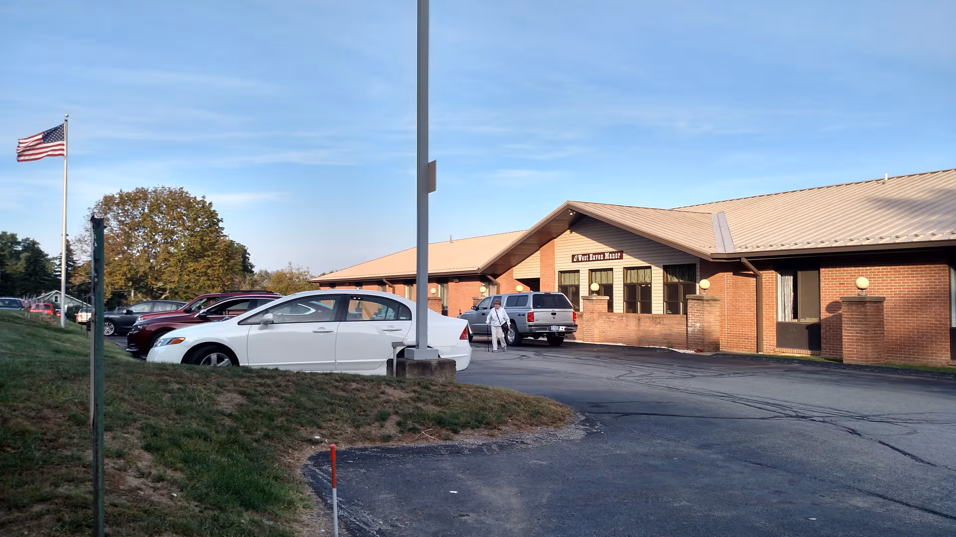 Brick senior living facility with parking lot and American flag in front.