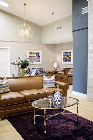 Modern senior living lounge with leather sofas, glass coffee table, and wall art.