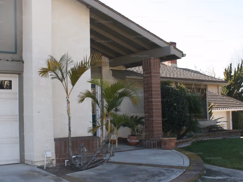 Residential building exterior with a curved walkway, potted palms, and a covered entrance.