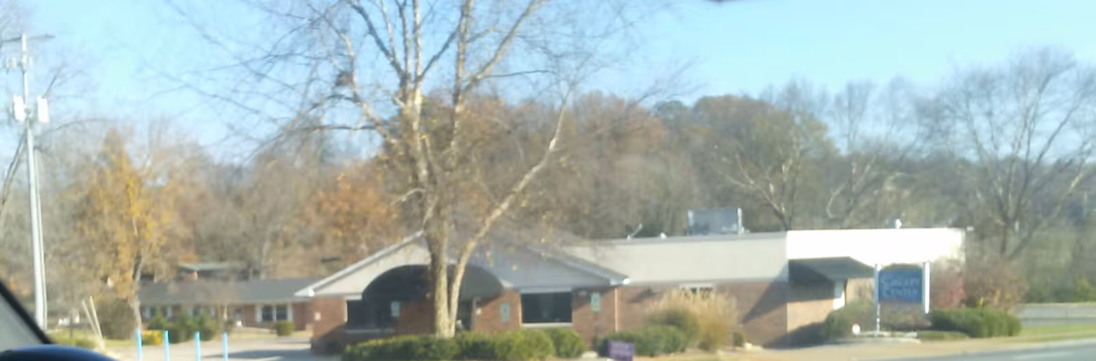 Exterior view of a single-story building with trees and a curved entrance in a parking lot