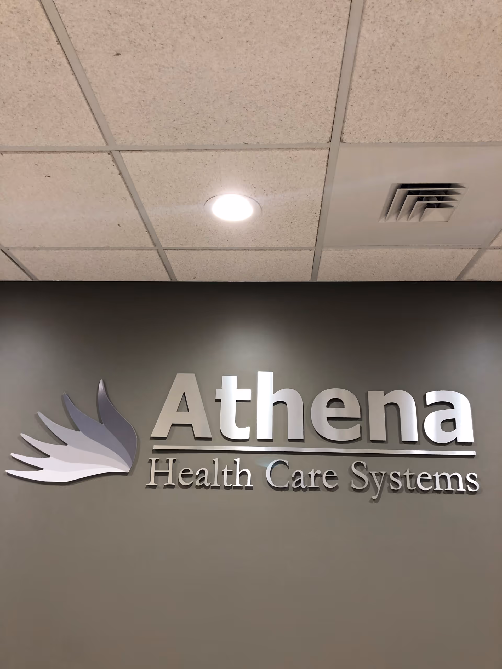 Indoor wall sign reading Athena Health Care Systems with ceiling tiles above