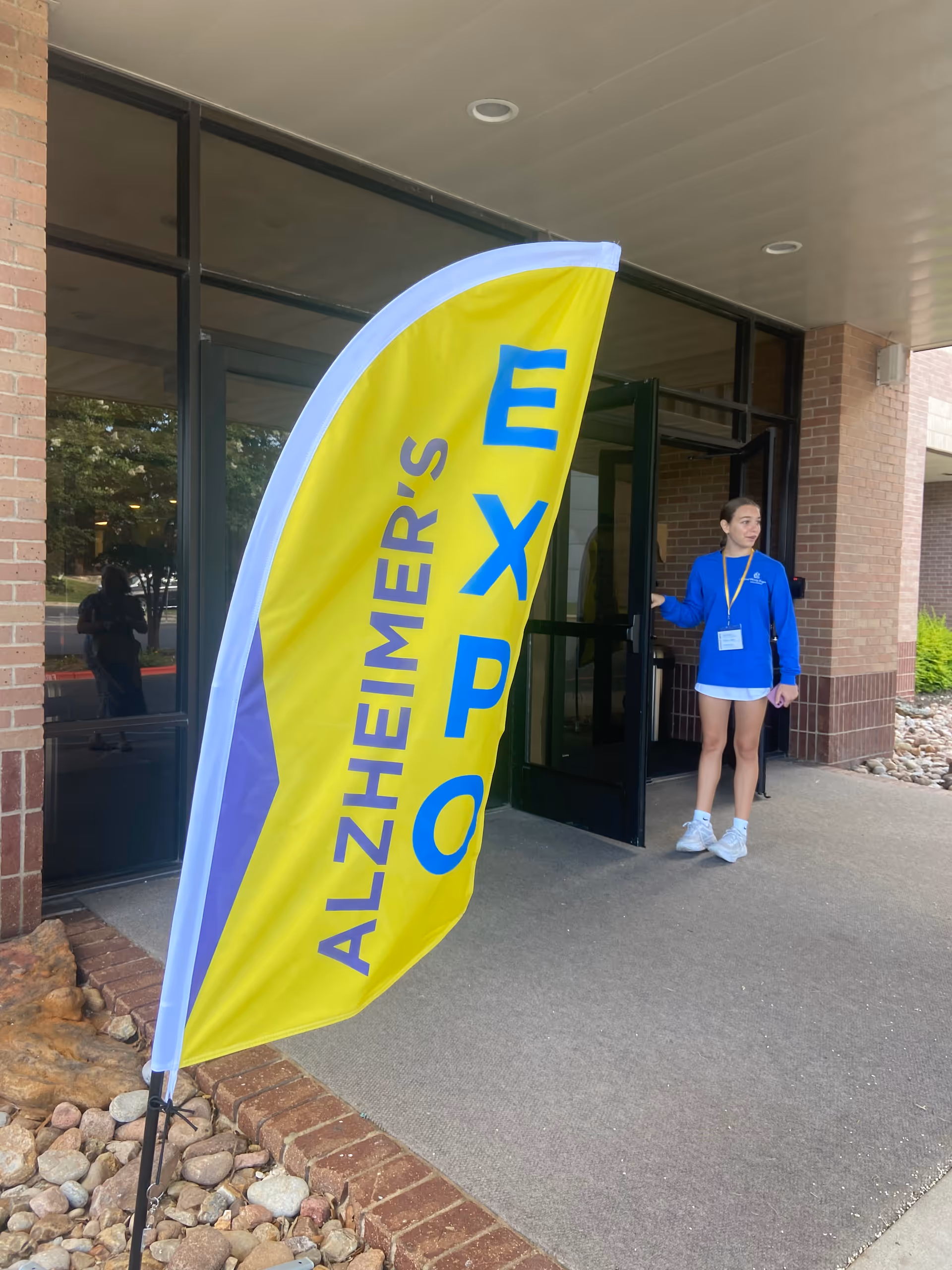 A staff member stands beside a bright Alzheimer's Expo banner at the facility entrance.