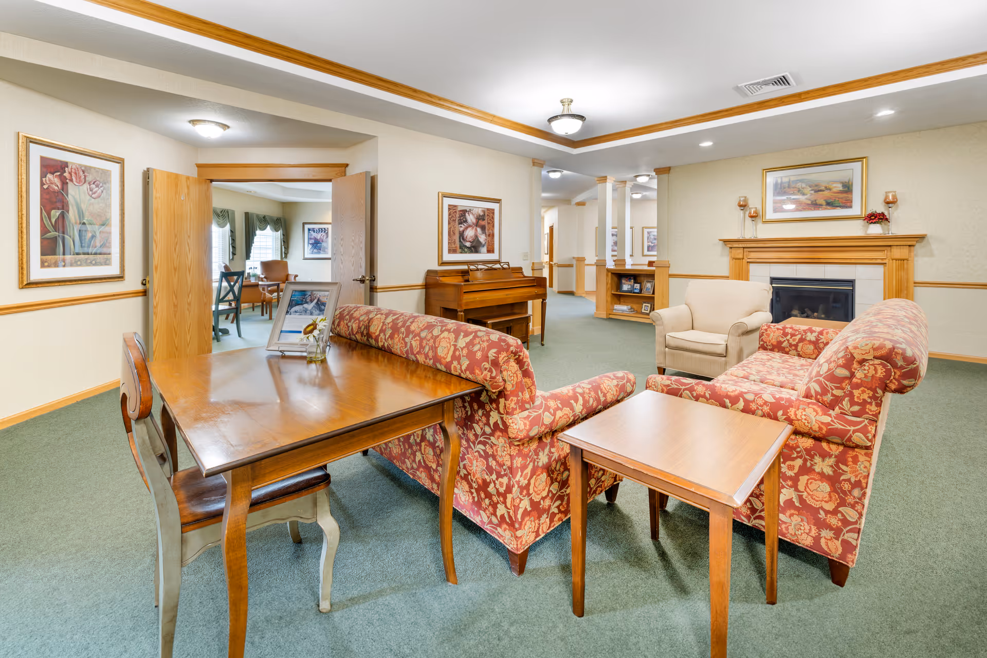 Spacious senior living room with red patterned sofas, a table, and a fireplace.