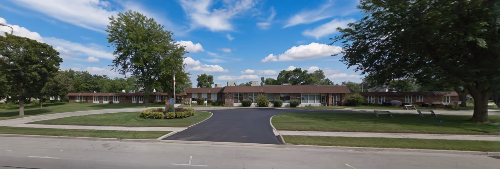 Brick, single-story senior care facility with a circular driveway, lawn, and trees.