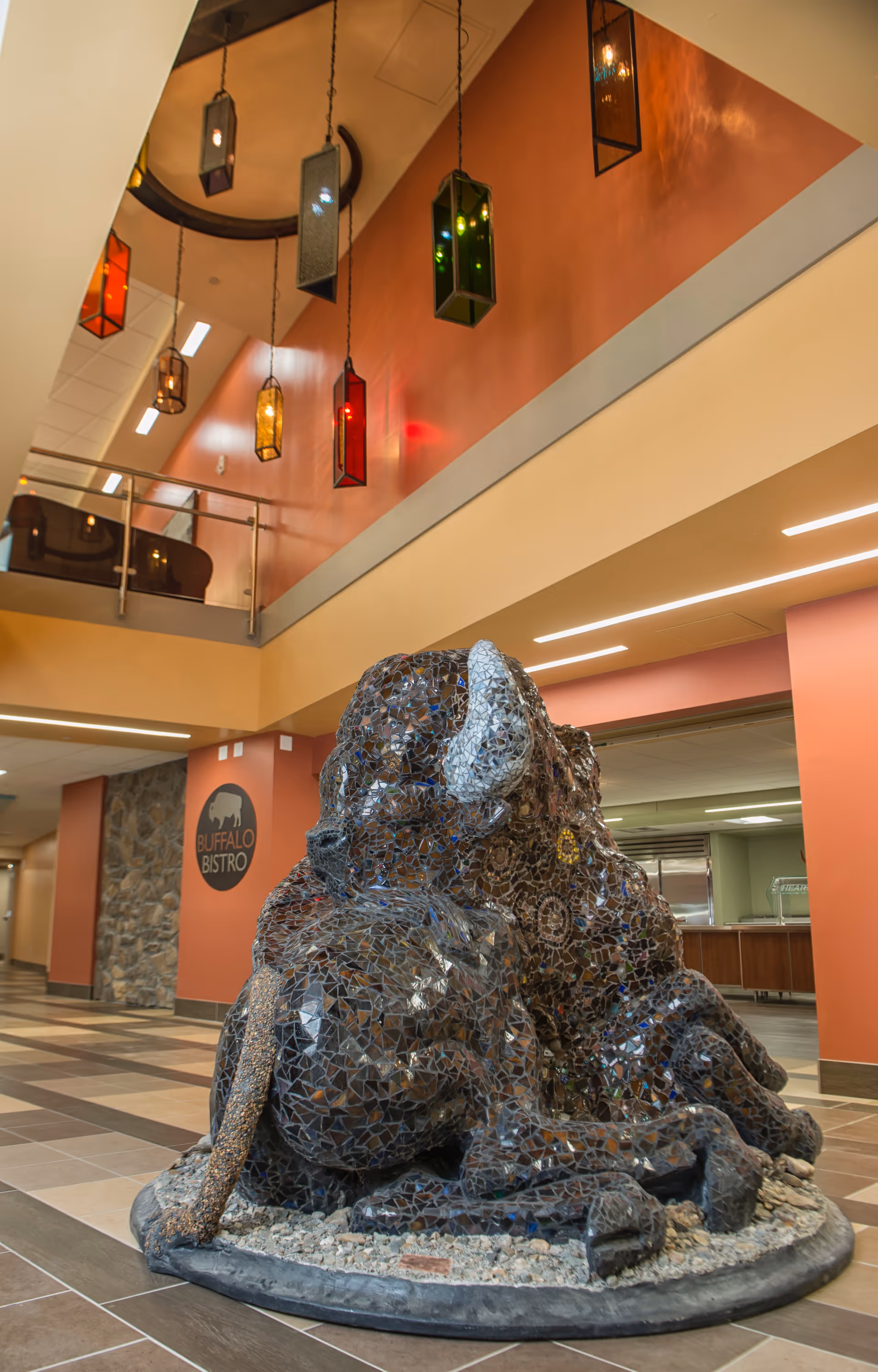 Interior lobby atrium with hanging decorative lights and a mosaic dog sculpture near Buffalo Bistro.