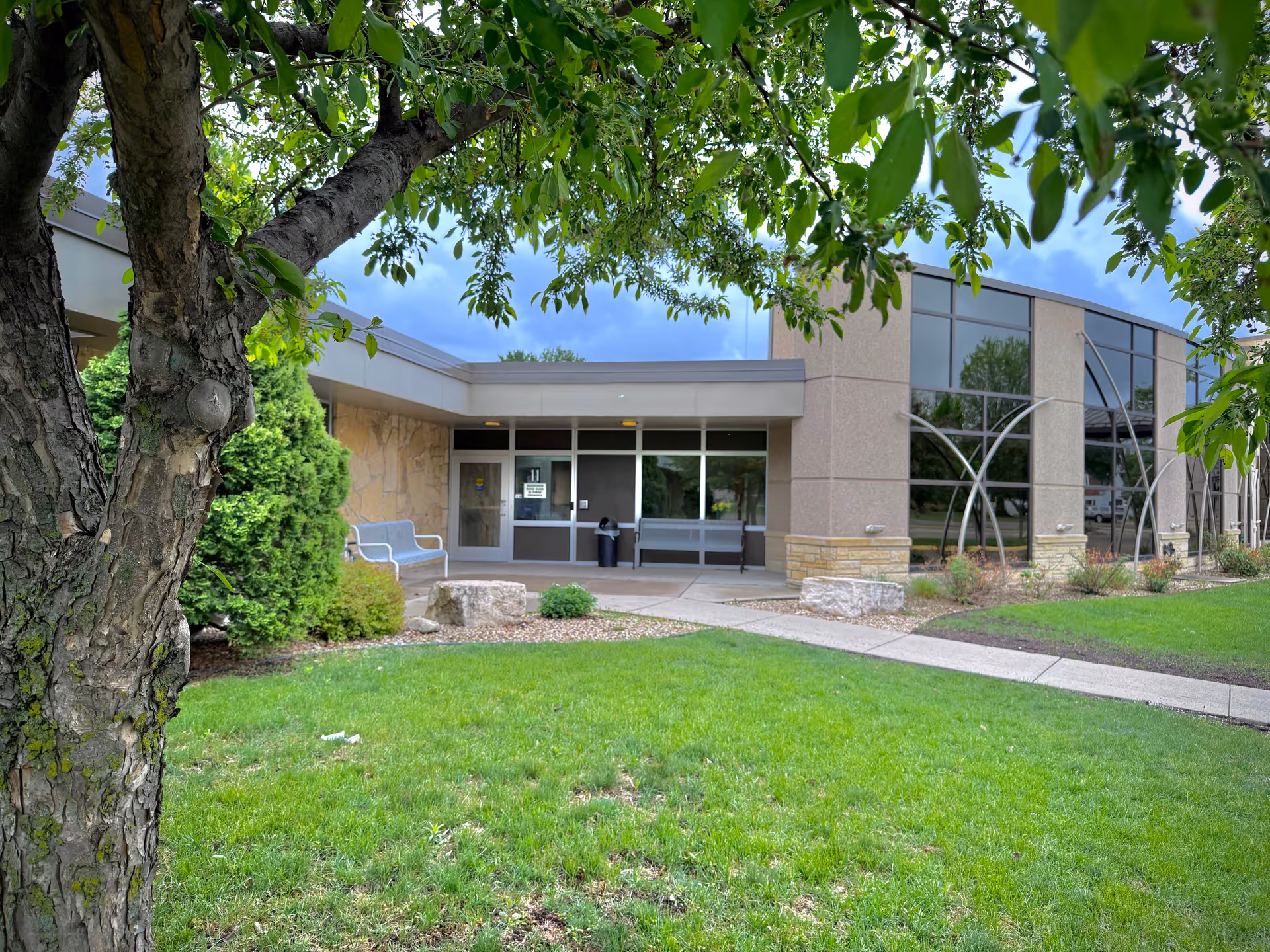 Exterior view of Cura of Le Sueur Nursing Home entrance, with glass doors and manicured lawn.