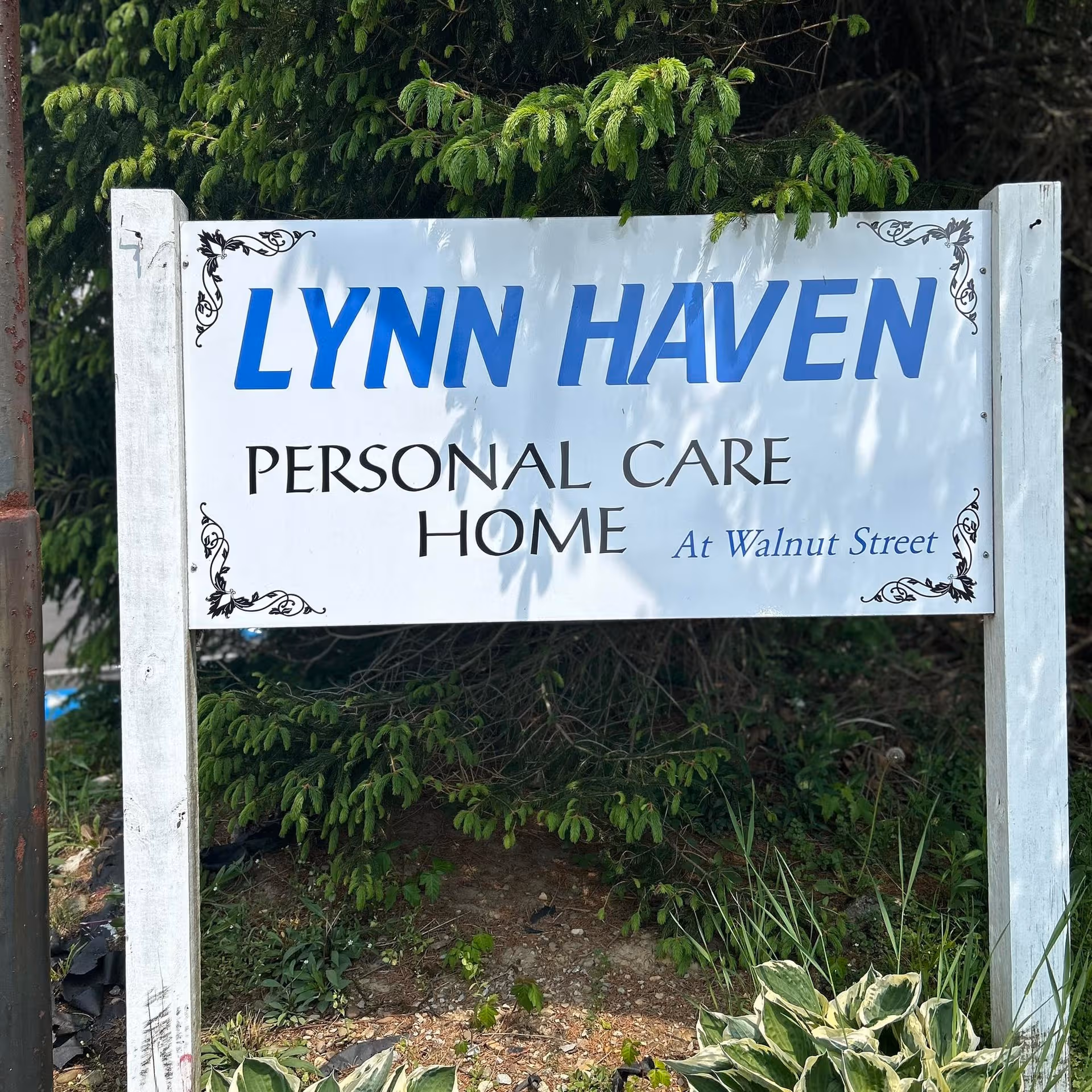 A white sign reads LYNN HAVEN PERSONAL CARE HOME with decorative corners, set near greenery.