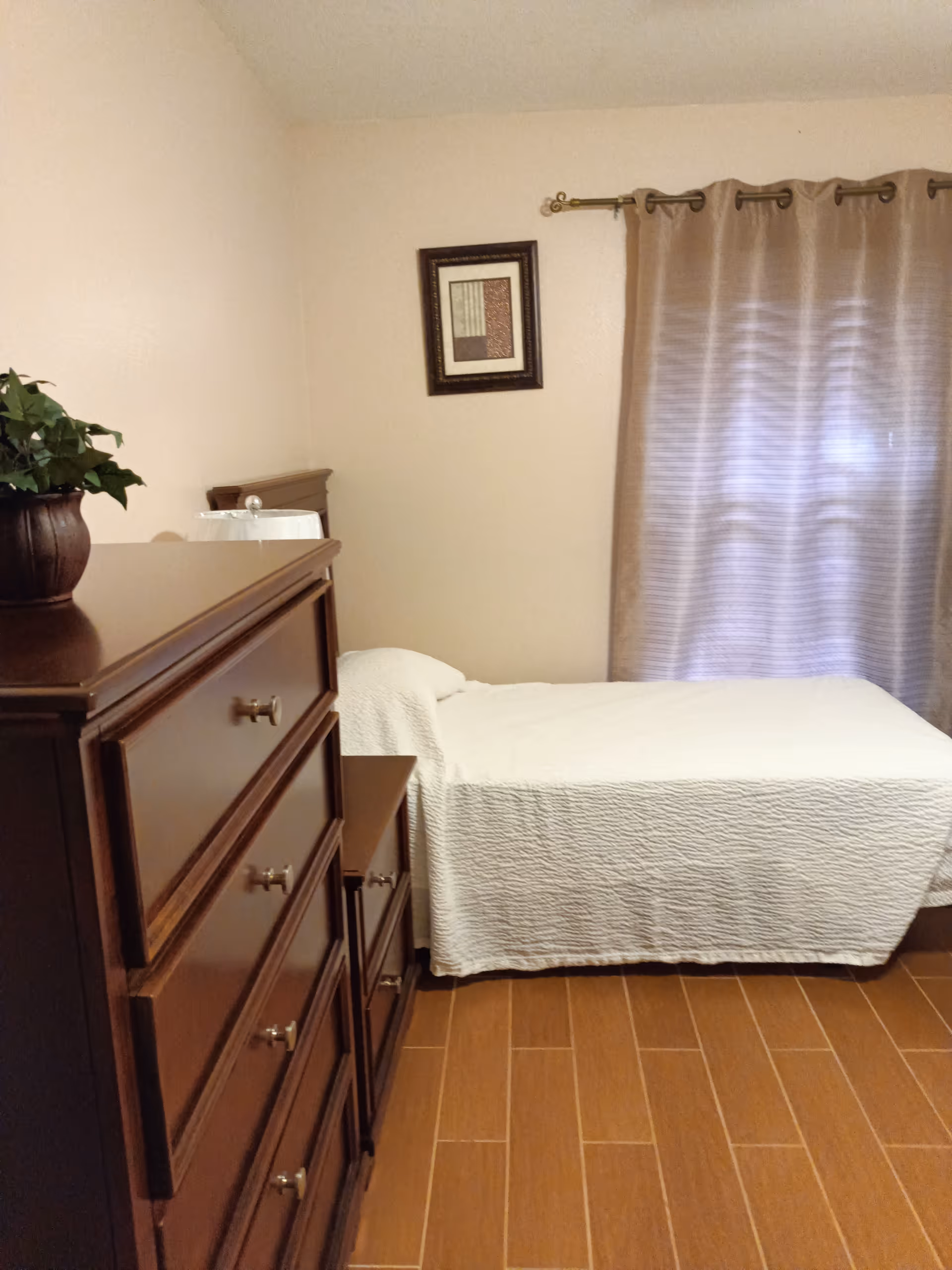 A bedroom in Vista Adult Family Care Home LLC with a bed, dresser, and curtain.