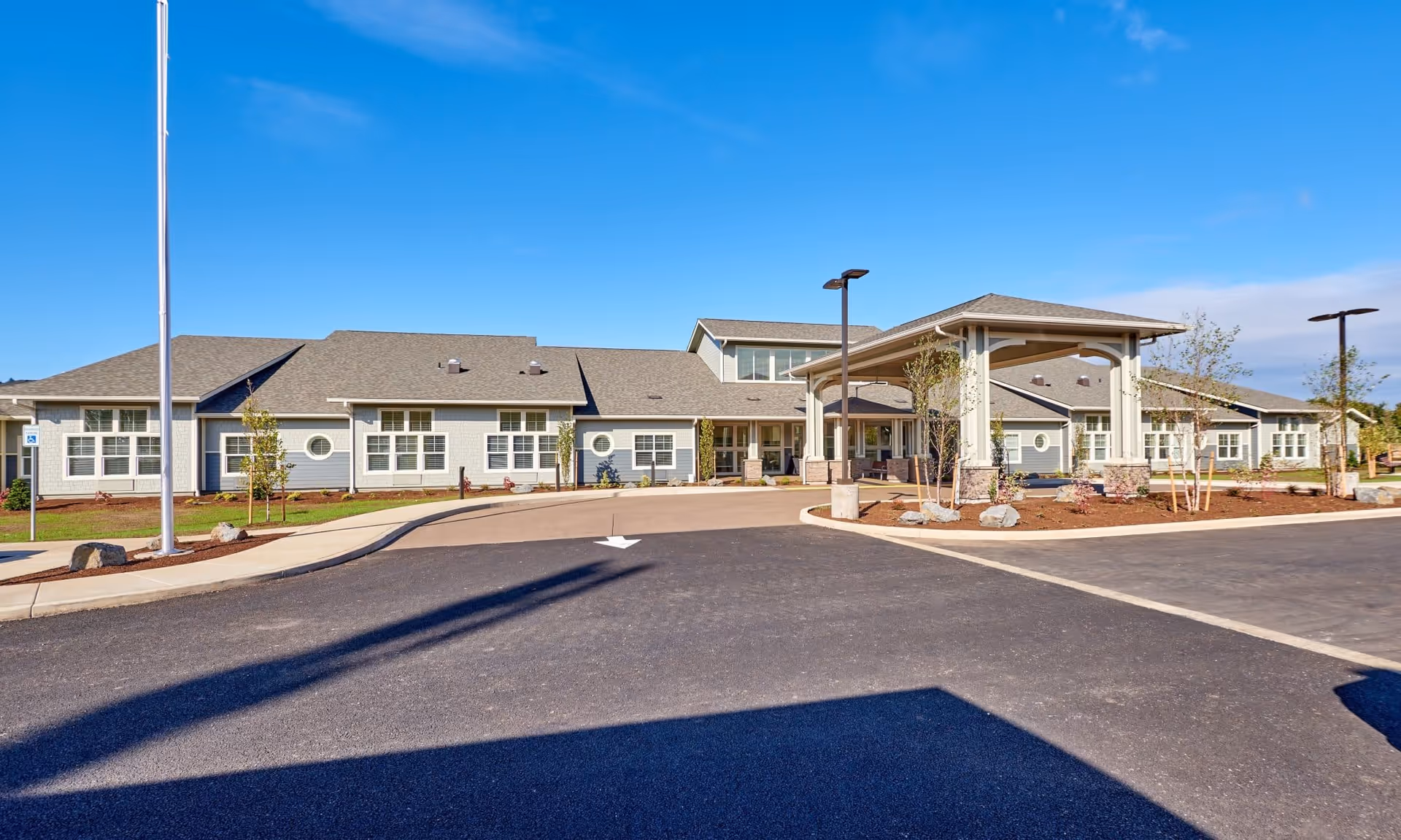 Front exterior of a single-story memory care facility with a covered entry, driveway, and landscaped grounds under a clear blue sky.