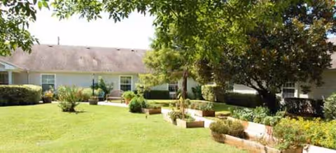 Exterior view of a single-story senior living campus with manicured lawn and trees.