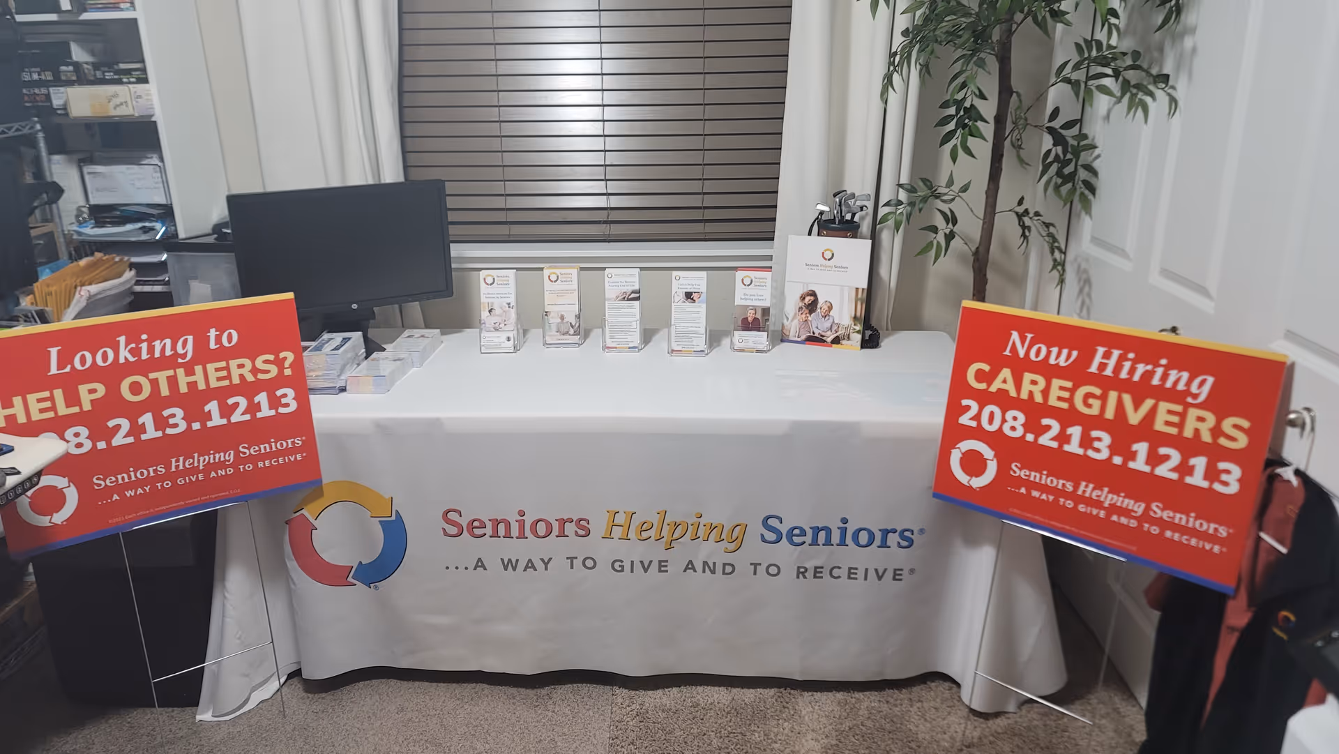 Indoor reception desk with a banner, pamphlets, and hiring signs for Seniors Helping Seniors Treasure Valley.