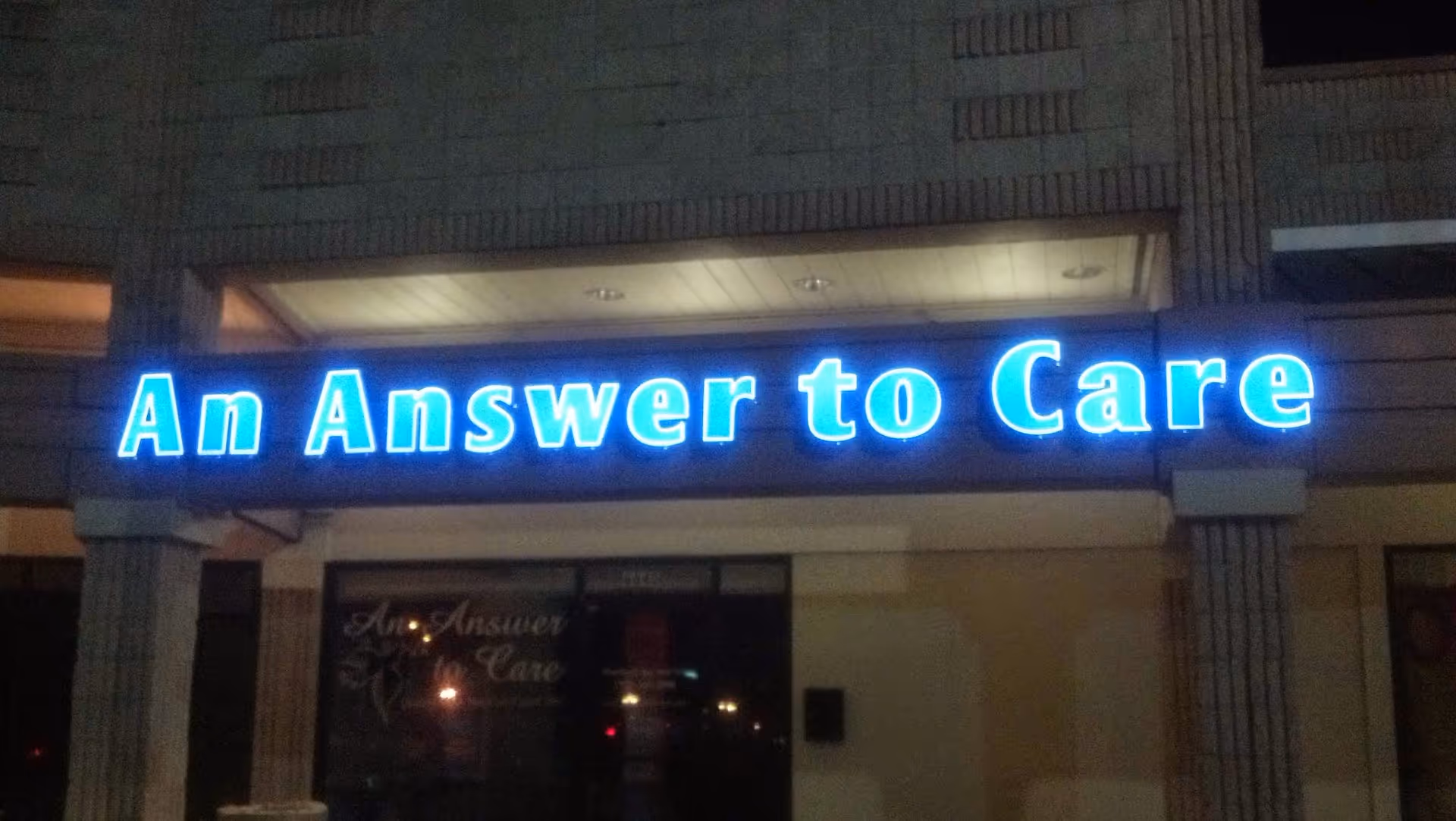 Nighttime exterior of a building with a bright blue neon sign reading An Answer to Care